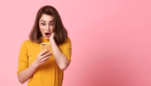 femme jeune, heureuse et surprise, belle  regarder, utilise un tlphone portable sur un fond rose avec de l'espace pour du texte.