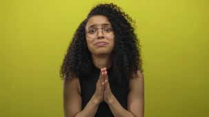 Jeune femme hispanique frottant ses doigts en studio sur un mur jaune avec un regard inquiet ; un appel dsespr  l'aide.