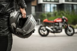 Un motard marche vers sa moto tenant son casque  la main.