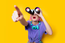 Jeune fille de style dans des v�tements violets avec des jumelles sur fond jaune. V�tements de style des ann�es 1980.