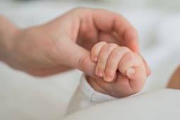 Un adulte tient la main d'un nourrisson.