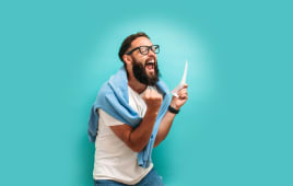 Jeune homme gagnant excit� et heureux ressentant de la joie en gagnant � la loterie, pla�ant des paris, recevant du cashback en ligne cadeau isol� sur fond bleu. Concept d'�motions du visage humain et de paris. Couleurs tendance.