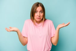 Jeune femme isol&eacute;e sur fond bleu, doutant et haussant les &eacute;paules dans un geste interrogateur.