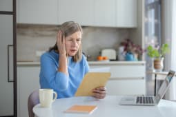 Une femme �g�e se couvrant l'oreille et paraissant anxieuse en lisant une facture.