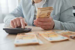 Un homme avec de l'argent et une calculatrice remplissant des papiers.