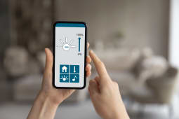 Gros plan sur une personne tenant un t&eacute;l&eacute;phone avec une application de maison intelligente sur l'&eacute;cran.