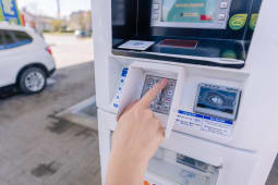 Une personne saisissant un code PIN sur un clavier &agrave; un terminal de paiement de station-service tout en ravitaillant une voiture.