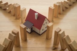 Maison entour&eacute;e de blocs de bois tombant comme des dominos.