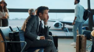 Homme d'affaires inquiet en costume assis seul &agrave; la porte de l'a&eacute;roport, perdu dans ses pens&eacute;es en attendant son vol, refl&eacute;tant le stress et l'incertitude du voyage d'affaires.