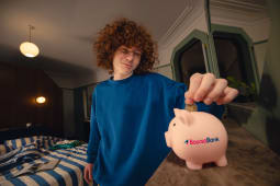 Un jeune met une pi&egrave;ce dans une tirelire Boursobank.