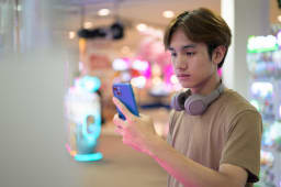 Jeune homme tha&iuml;landais utilisant un distributeur automatique dans un centre commercial avec des &eacute;couteurs