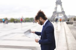 Homme en costume lit un journal devant la tour Eiffel.
