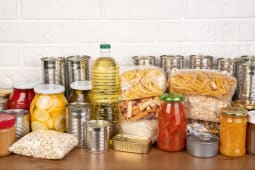 Des dons de nourriture tels que des p&acirc;tes, du riz, de l'huile, du beurre de cacahu&egrave;te, des conserves, de la confiture et autres sur une table brune.