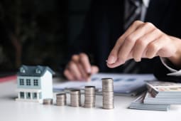 Une maison miniature et des piles de pi&egrave;ces de monnaie.