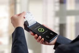 Client tenant un terminal de paiement portable avec un re&ccedil;u imprim&eacute; et un &eacute;cran de paiement approuv&eacute;, repr&eacute;sentant un encaissement r&eacute;ussi, l'ach&egrave;vement d'une transaction de vente au d&eacute;tail et des syst&egrave;mes de paiement &eacute;lectroniques modernes