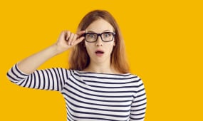 Jeune &eacute;tudiante tr&egrave;s surprise par quelque chose. Belle jeune femme nerd en haut ray&eacute; et lunettes isol&eacute;e sur fond jaune regardant la cam&eacute;ra avec une expression faciale dr&ocirc;le, choqu&eacute;e, &eacute;tonn&eacute;e