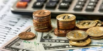 Des pi&egrave;ces de bitcoin, des dollars et une calculatrice sur table.