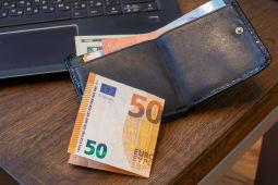 Portefeuille en cuir noir avec un billet de 50 euros sur un bureau en bois &agrave; c&ocirc;t&eacute; d'un ordinateur portable. Finance, budget personnel, paiement en ligne. Photo r&eacute;elle