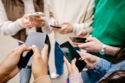 Plusieurs personnes tiennent et utilisent des smartphones ensemble dehors.