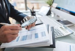 Homme examine des documents financiers avec une loupe au bureau.