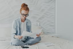 Une belle femme rousse freelance regarde attentivement les documents, calcule et g&egrave;re les finances