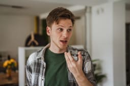 Jeune homme enregistrant un message vocal sur un smartphone &agrave; l'int&eacute;rieur