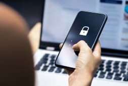 Main tenant un smartphone verrouill&eacute; devant un ordinateur portable.