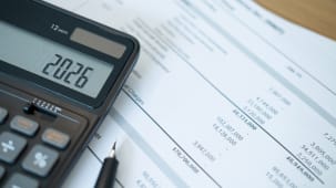 Calculatrice affichant 2026, documents financiers et stylo pr&eacute;sents.