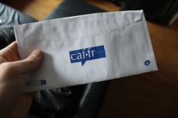 caf.fr, a hand holding an envelope with a partial view of the logo caf.fr Caisse d'Allocation Familiale on it. Translation of French: family allowance fund.