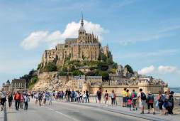 De nombreux touristes marchent vers le Mont-Saint-Michel sous le soleil.