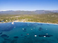 Plage de sable, mer turquoise, bateaux, for&ecirc;t, montagnes en arri&egrave;re-plan.