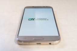 Logo de Cr&eacute;dit Agricole sur l'&eacute;cran du smartphone en gros plan sur fond blanc