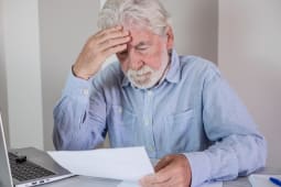 Un vieil homme paraissant stress&eacute; en lisant des documents &agrave; son bureau.