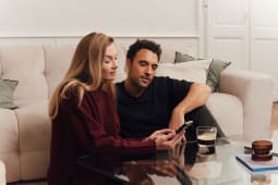Un couple assis regarde un t&eacute;l&eacute;phone dans un salon cosy.