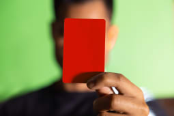 Une main tient un carton rouge devant un fond vert.