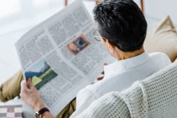 Homme assis lisant un journal dans un fauteuil confortable.