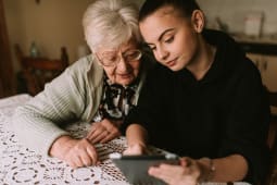 La grand-m&egrave;re caucasienne &acirc;g&eacute;e et sa belle petite-fille adolescente regardent les photos sur la tablette dans la pi&egrave;ce.