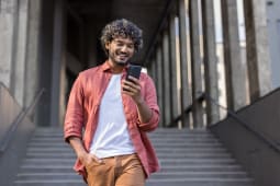 Un jeune debout pr�s d'un b�timent, la main dans la poche et utilisant un t�l�phone portable.