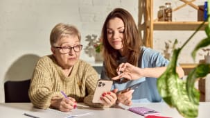 Femme aidant sa m�re senior avec un transfert d'argent mobile � la maison. Concept de finance familiale, banque en ligne, soutien aux a�n�s, �ducation fintech et paiement num�rique s�curis�.