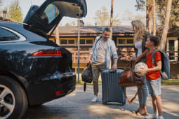Une famille range des bagages dans le coffre d'une voiture.