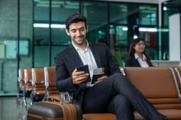 Un homme d'affaires caucasien utilise un t&eacute;l&eacute;phone mobile intelligent en attendant dans le salon d'affaires de la compagnie a&eacute;rienne en attendant l'embarquement pour l'utilisation de l'avion.