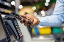 Personne effectuant une transaction num&eacute;rique &agrave; l'aide d'un t&eacute;l&eacute;phone mobile &agrave; une caisse, montrant la technologie NFC moderne pour un paiement sans esp&egrave;ces sans faille dans un environnement de vente au d&eacute;tail