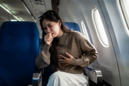 Une femme se tenant sa poitrine, assise pr&egrave;s du hublot dans un avion.