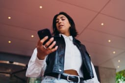 �tudiante espagnole v�rifiant les horaires de transport sur une application smartphone. Femme hispanique envoyant des messages texte sur l'�cran de son t�l�phone mobile pr�s d'un pavillon de construction architecturale moderne dans un couloir.