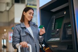 Voyageuse heureuse utilisant sa carte de cr&eacute;dit au distributeur automatique &agrave; l'a&eacute;roport.