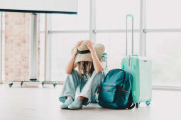 Jeune femme assise dans un terminal d'a&eacute;roport avec des bagages assise la t&ecirc;te entre les mains.