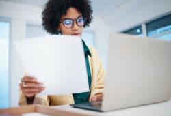 Une femme devant un ordinateur portable tenant des documents.