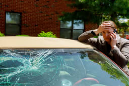 Une femme passant un appel t&eacute;l&eacute;phonique &agrave; c&ocirc;t&eacute; d'une voiture dont le pare-brise est endommag&eacute;.