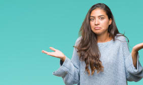 Jeune belle femme arabe portant un pull d'hiver sur un fond isol&Atilde;, expression perplexe et confuse avec les bras et les mains lev&eacute;s. Concept de doute.