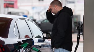 Un homme faisant le plein de sa voiture, l'air inquiet.